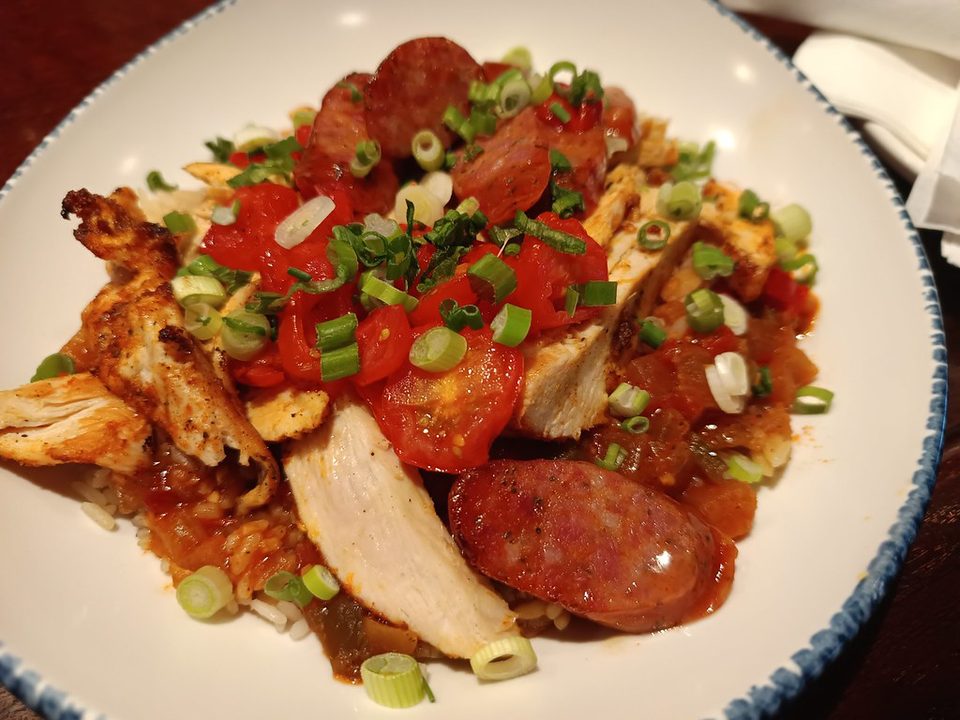 Sliced smoked sausage and grilled chicken over rice with tomatoes and scallions on a white plate