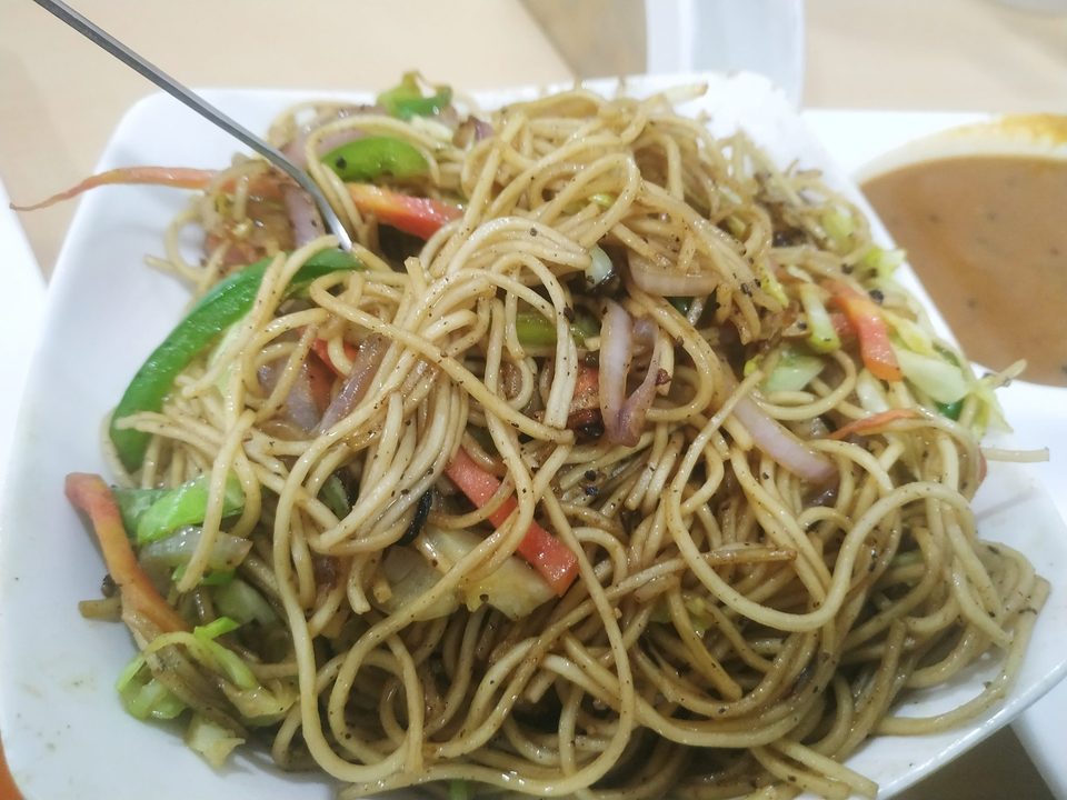 Noodles tossed with sliced cucumber, carrot and onion beside a small dish of sauce