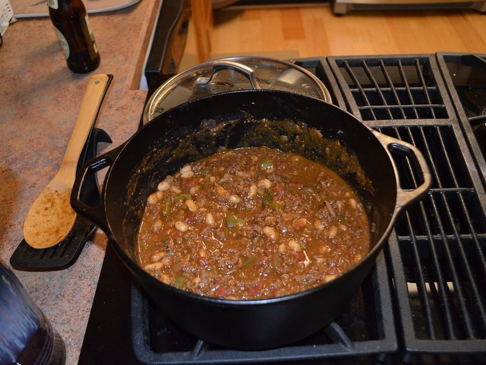 Pot of hearty chili with beans simmering in a cast-iron Dutch oven on the stove